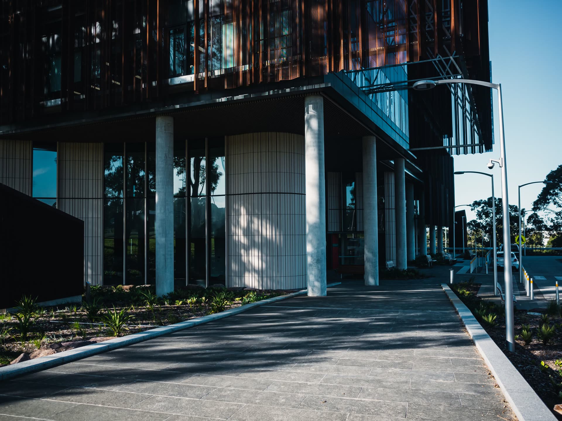 Exterior walkway and sheltered ground-floor entrance of a contemporary healthcare building, photographed in daylight. Contextual architecture photography, not a specific facility.